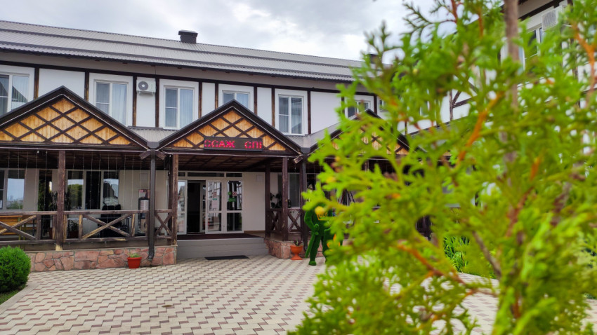 Фасад здания с входом под навесом и красной световой вывеской за ветвями