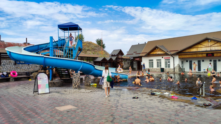 Открытый термальный бассейн с синей водной горкой и отдыхающими у раздевалок
