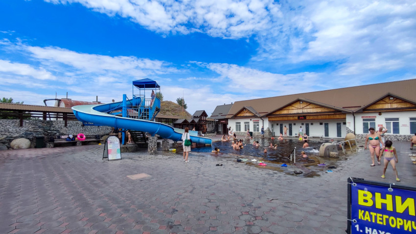 Открытый бассейн с водной горкой на фоне корпусов и яркого летнего неба