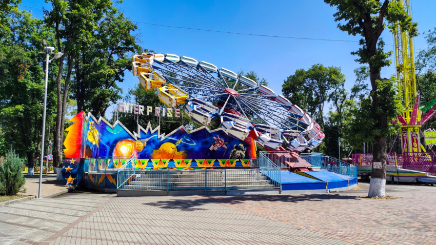 Аттракцион Enterprise на площади парка с деревьями вокруг
