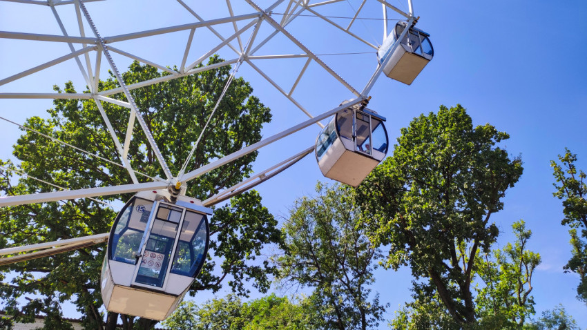 Кабинки колеса обозрения среди спиц на фоне зелёных деревьев