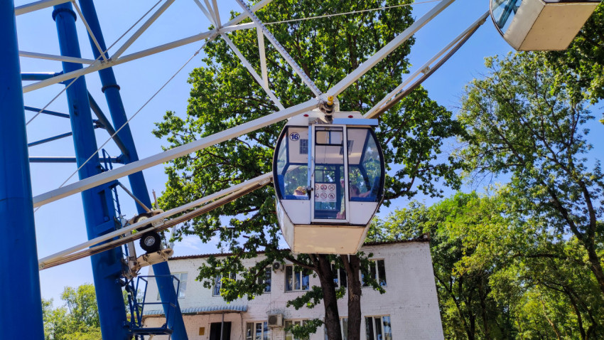 Кабинка колеса обозрения над зданием и деревьями крупным планом