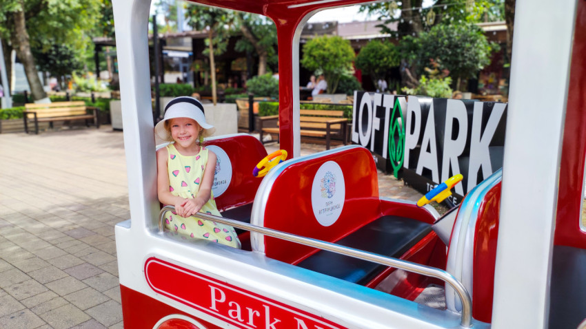 Девочка позирует у детского аттракциона рядом с вывеской LOFT PARK в Городском парке Нальчика