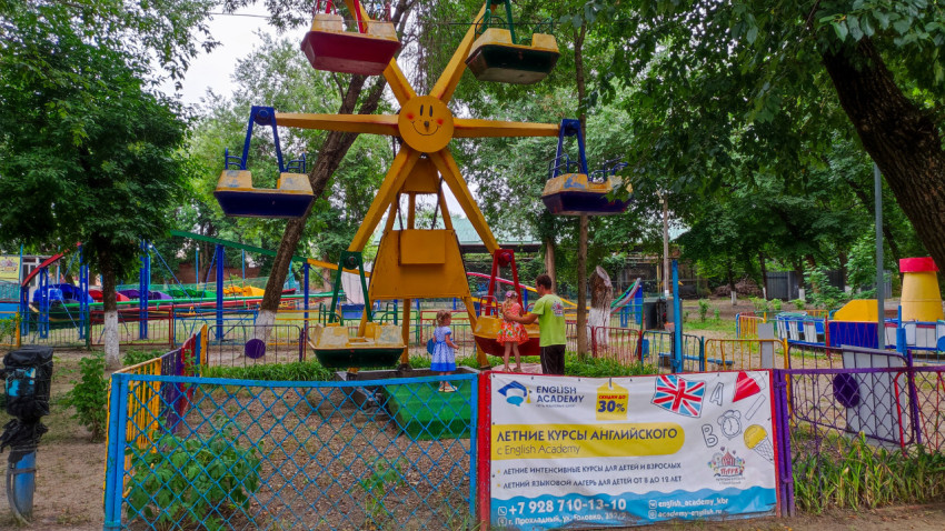 Детское колесо обозрения в парке и рекламный баннер летних курсов English Academy