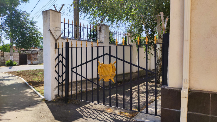 Кованые ворота с эмблемой и колючей проволокой у ведомственного ограждения