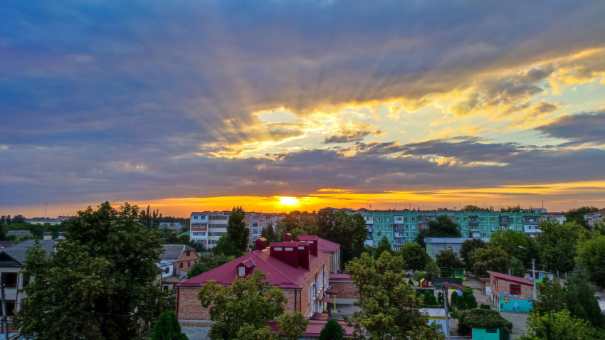 Закатные лучи над жилым районом с панельными домами и зелёными деревьями