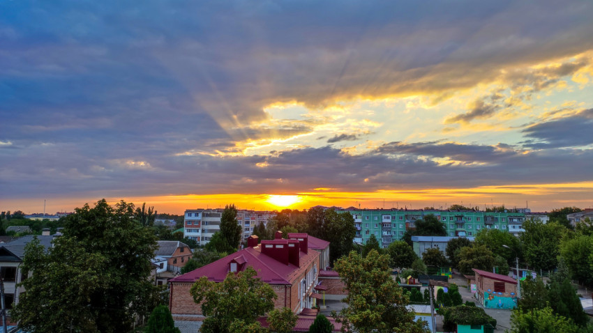 Яркое солнце у горизонта и контрастные облака над жилым районом