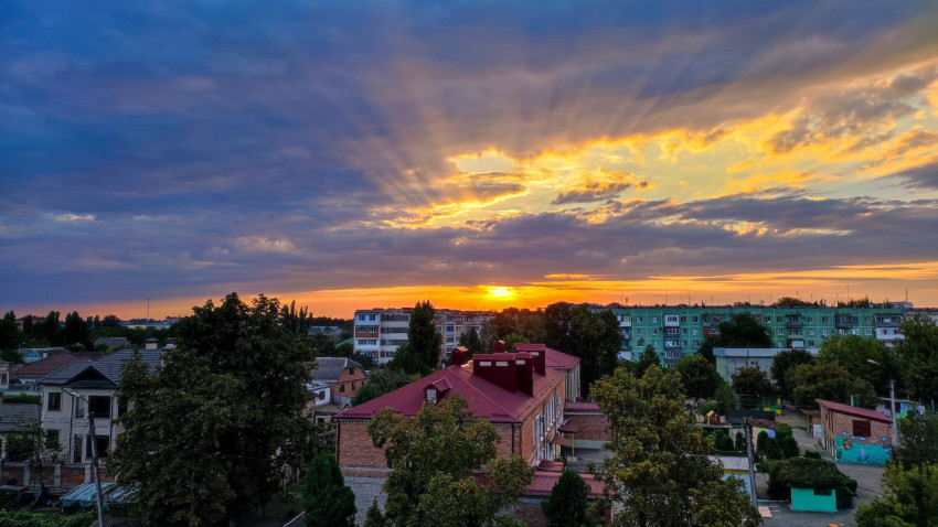 Золотая подсветка облаков и лучи солнца над городским жилым массивом