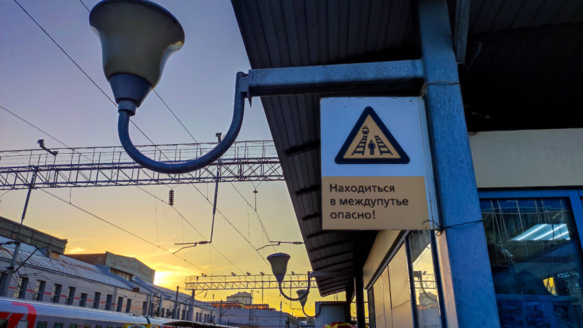 Предупреждающий знак безопасности на платформе на фоне закатного неба и проводов