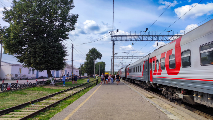 Пассажирский поезд РЖД у платформы, зелёная зона и станционные постройки вдоль путей