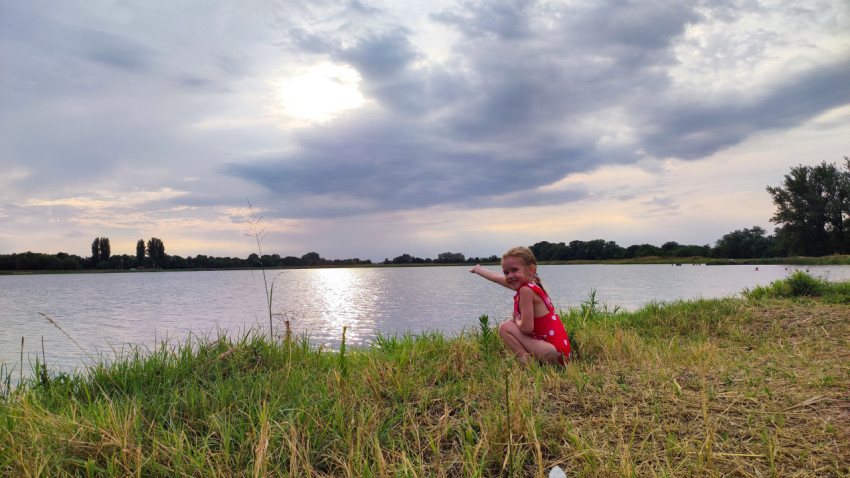 Девочка на берегу показывает на воду и солнечные блики