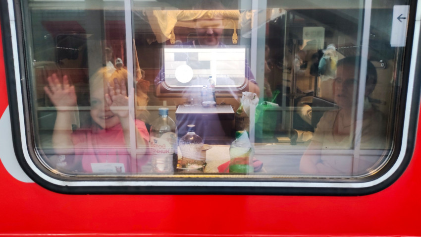 Пассажиры в купе, вид через окно вагона: ребёнок машет рукой на станции