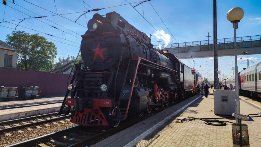 Паровоз ЛВ-0233 с красной звездой на платформе рядом с пассажирскими вагонами