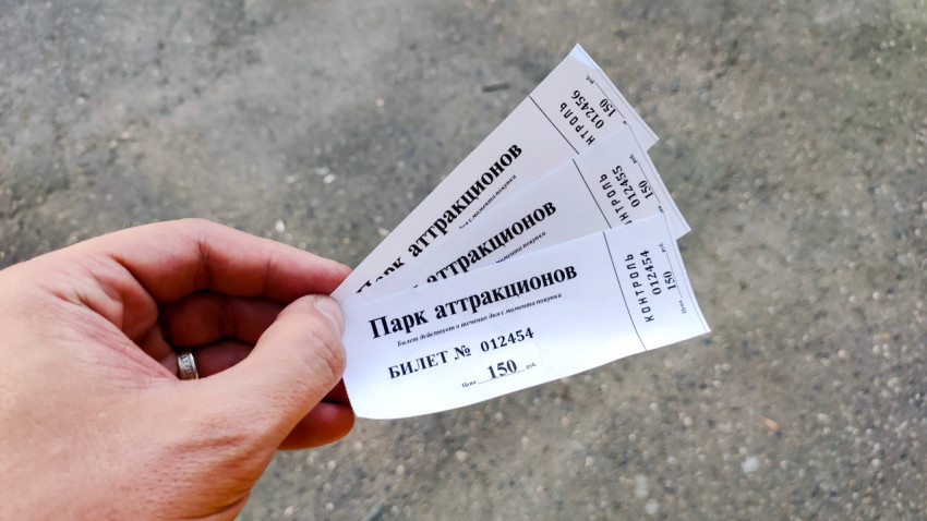 Бумажные билеты в парк аттракционов в руке на фоне асфальта