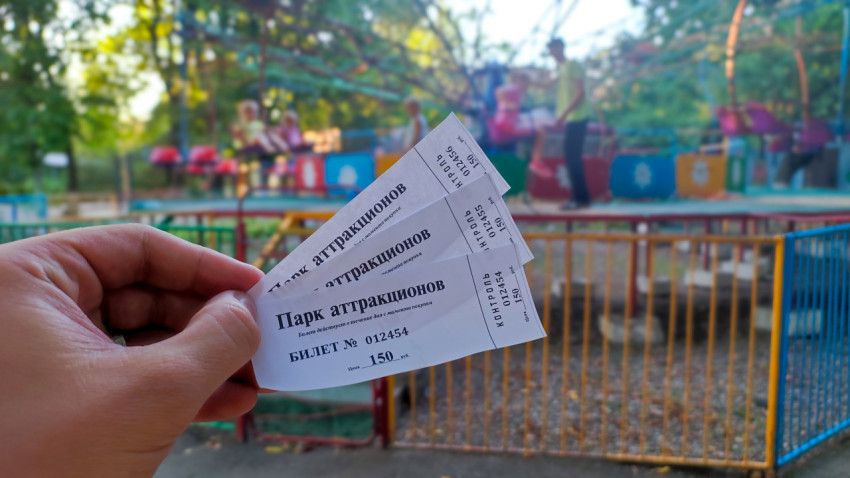 Билеты в парк аттракционов на фоне работающего аттракциона за ограждением