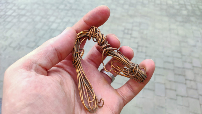 Скрученная медная проволока в руке на фоне тротуарной плитки