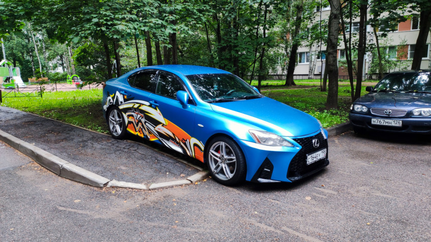Синий седан Lexus с яркой виниловой оклейкой и кастомными дисками на парковке у жилого дома