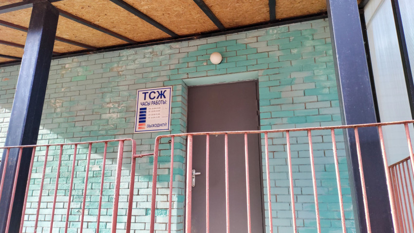 Вход в офис ТСЖ с табличкой на кирпичной стене и перилами