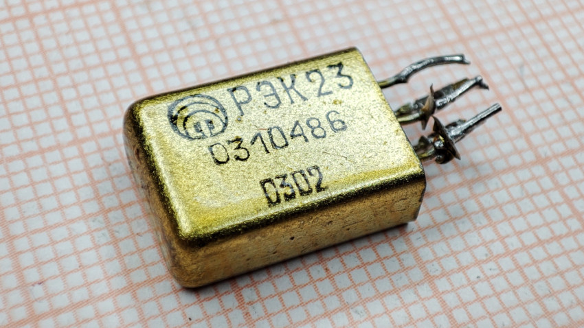 Реле РЭК23 с маркировкой и изогнутыми выводами на фоне миллиметровки