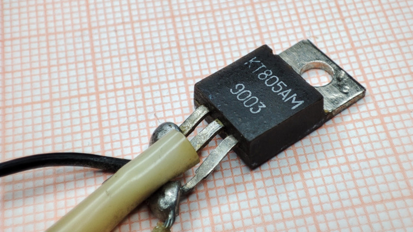 Транзистор КТ805АМ с припаянными проводами на фоне миллиметровой бумаги