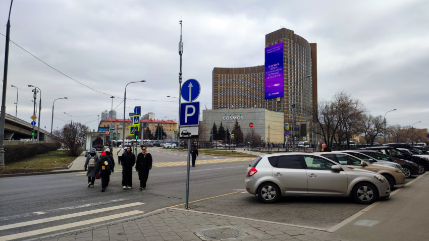 Группа людей идет по улице рядом с припаркованными автомобилями