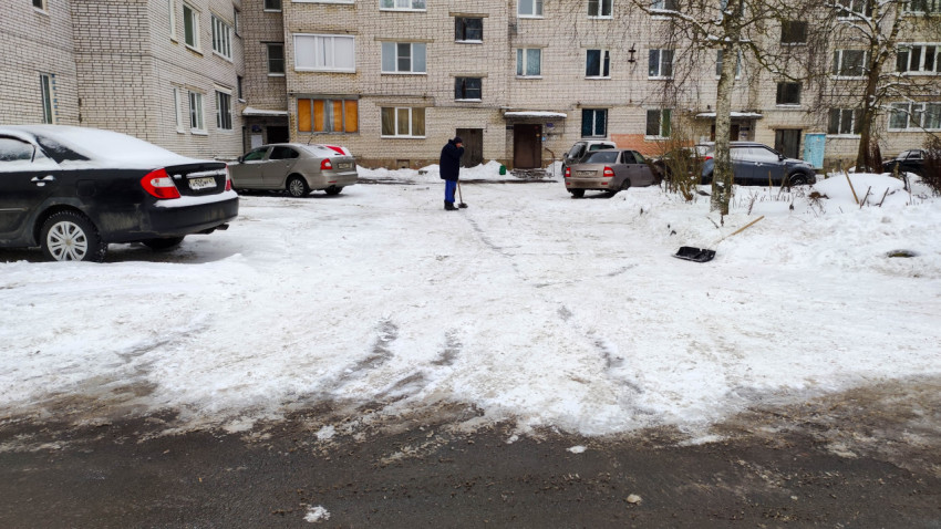 Человек убирает снег во дворе многоквартирного дома в зимнее утро