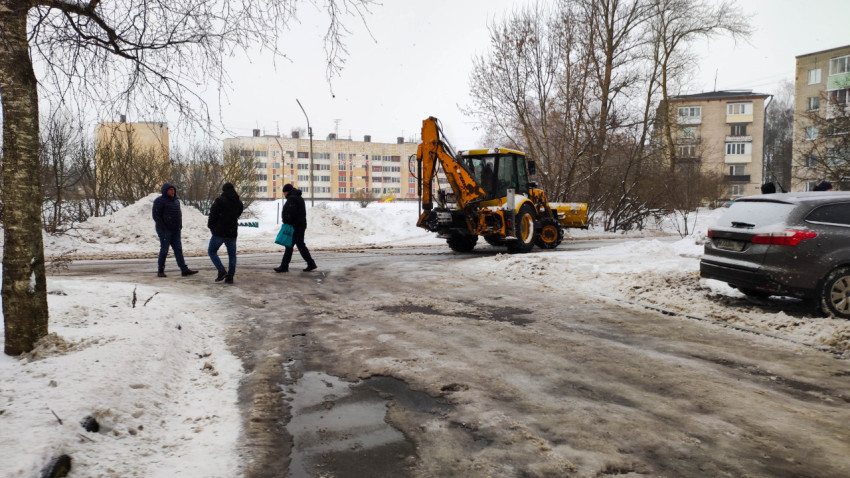 Трактор убирает снег с дороги во дворе жилого комплекса зимой