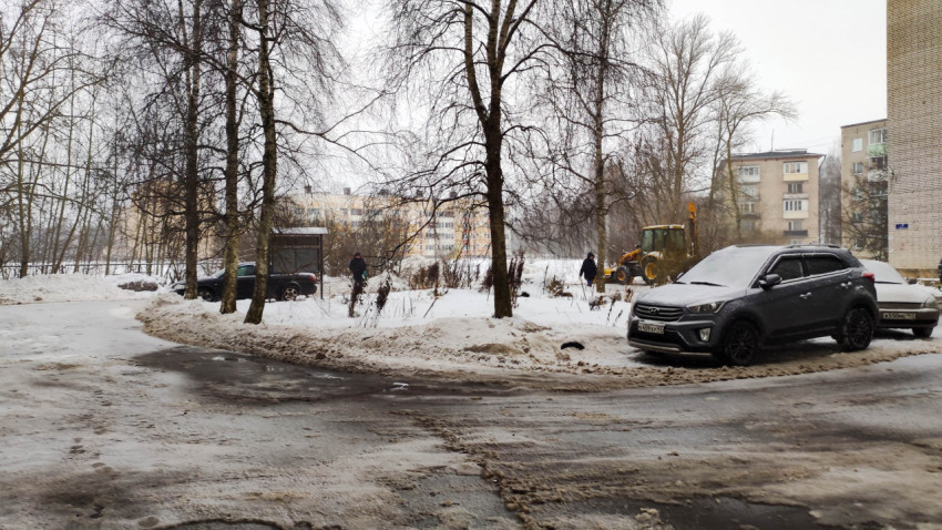 Трактор очищает снег с дороги во дворе жилых зданий