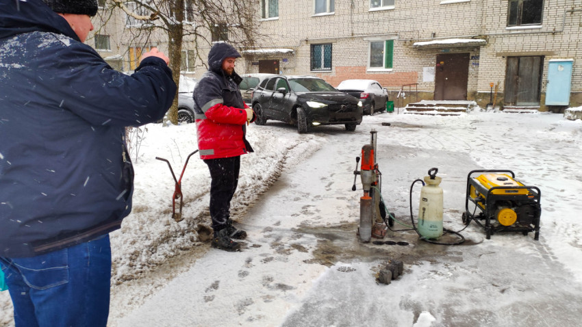 Ремонт дороги зимой во дворе дома работниками и техникой