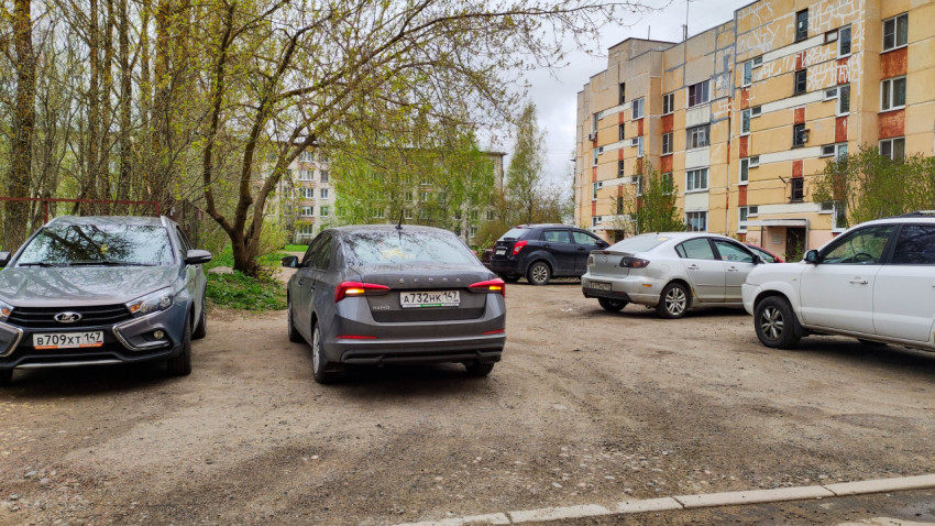 Парковка во дворе жилых домов с автомобилями и зелеными деревьями