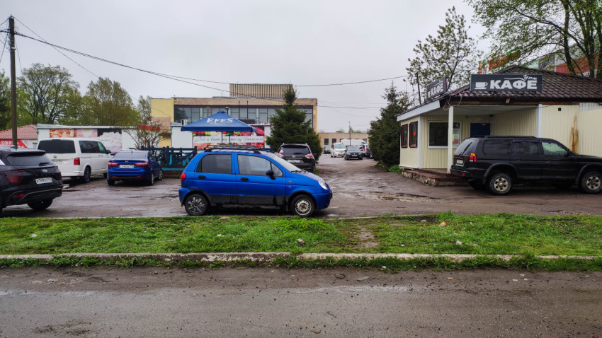 Маленькая синия машина на парковке у кафе в дождливый день