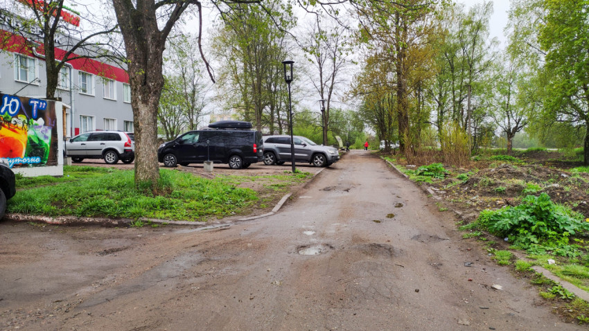 Дорога с ямами и припаркованными автомобилями в городе