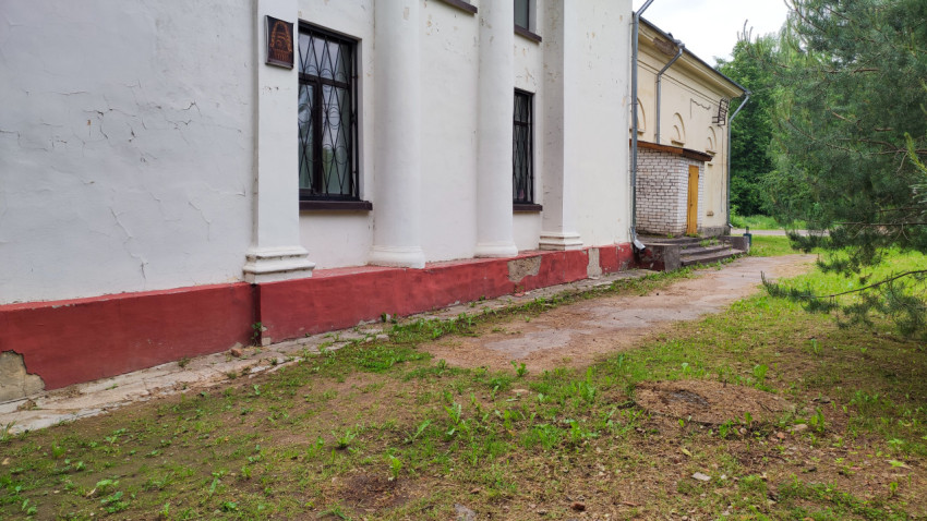 Угол старого здания с потрескавшейся краской и зеленой травой