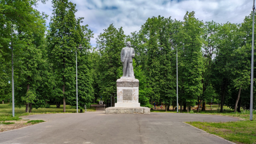 Памятник Ленину в парке Порхов, окруженный зелеными деревьями