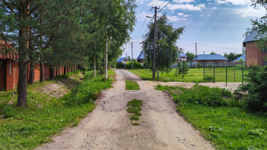 Тихая деревенская дорога летом среди зелени и облаков
