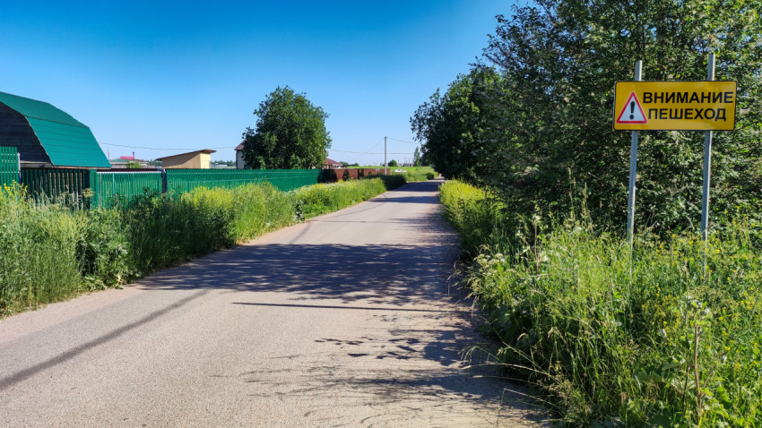 Дорога в пригороде с зелеными насаждениями и дорожным знаком