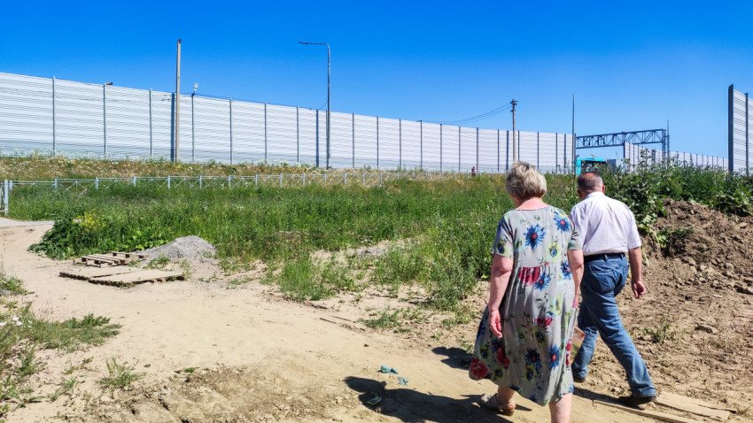 Пара прогуливается по зелёному полю рядом с высоким забором