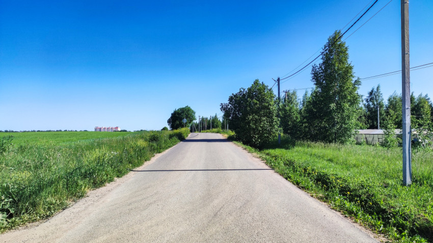 Тихая дорога между зелеными полями в ясный солнечный день