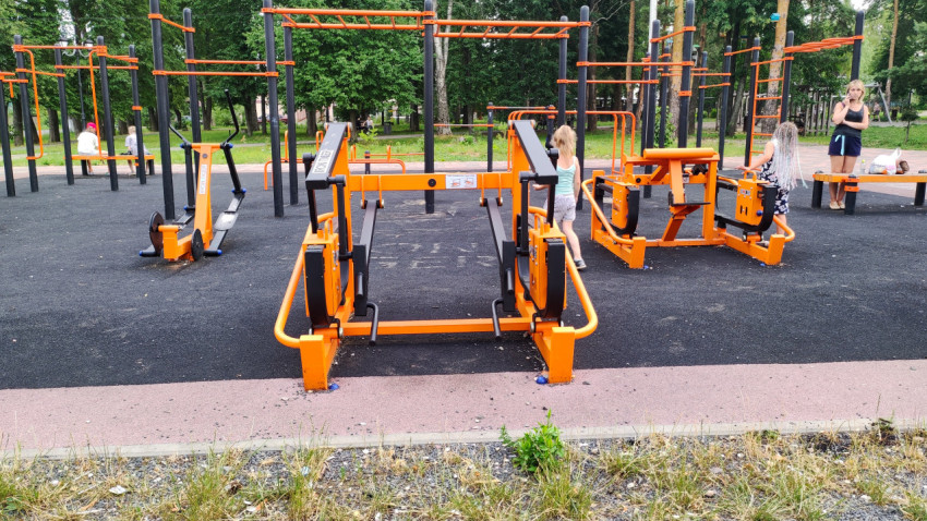 Открытая спортивная площадка с тренажерами и отдыхающими в парке