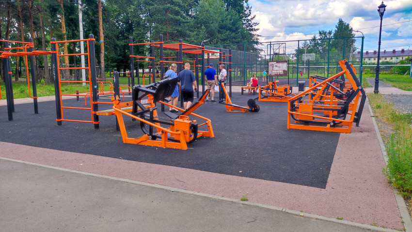 На спортивной площадке люди занимаются на уличном тренажёре в теплую погоду