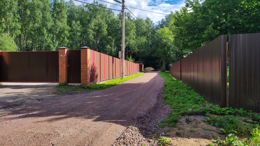 Дорога в поселке среди зеленых насаждений и заборов