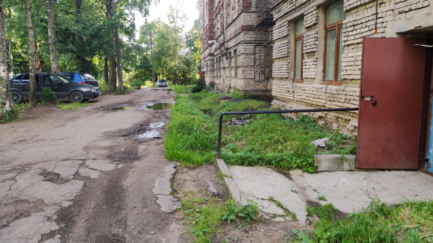Упадок территории жилого дома с грязной дорогой и неухоженным входом в подъезд
