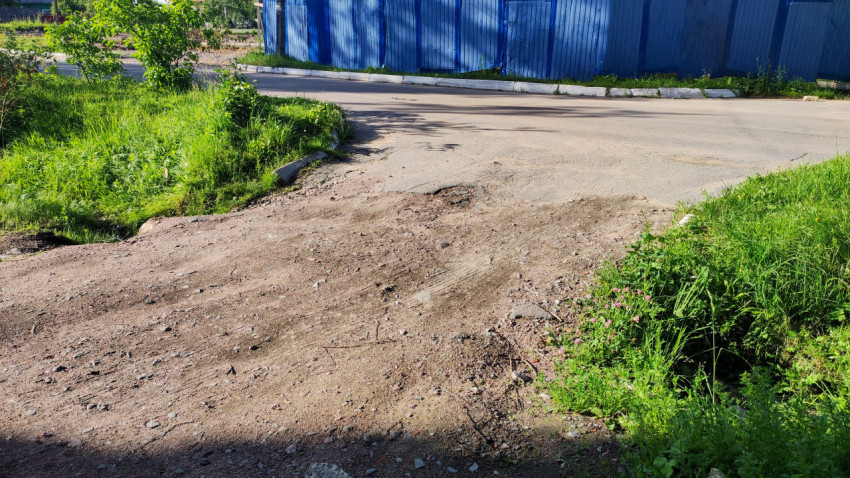 Дорога над водопропускной трубой, окруженная кустарником и забором
