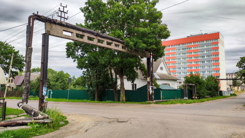 Трубопровод над дорогой в жилом районе с многоэтажным домом на фоне