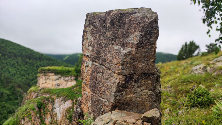 Каменная скала на фоне зелёных холмов в облачный день