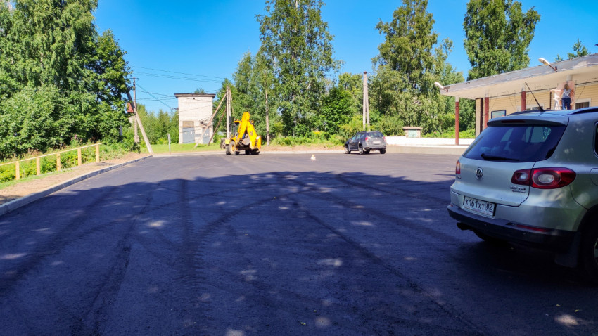 Асфальтированная площадка с несколькими автомобилями и экскаватором-погрузчиком