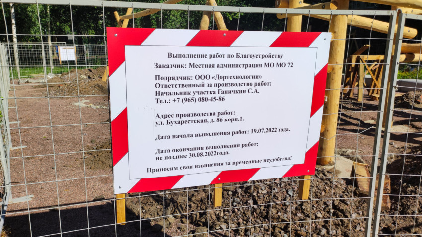 Табличка с текстом на заборе на фоне строящейся детской площадки