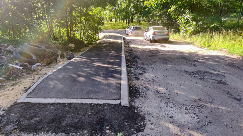 Асфальтированная пешеходная дорожка вдоль разбитой дорогиalt footpath along a broken road where cars are moving