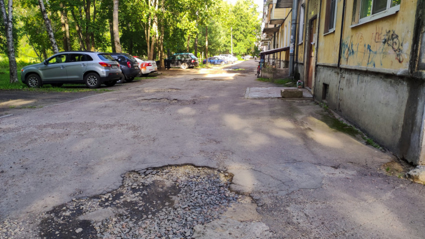 Двор старого дома с ямами на дороге и припаркованными машинами
