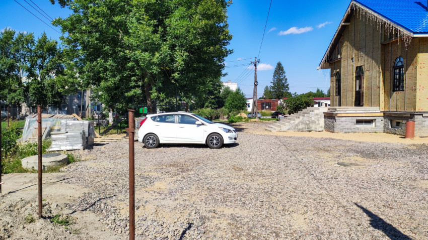 Белый Hyundai Solaris припаркован на гравийной площадке рядом с домом